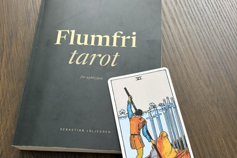 Boken Flumfri tarot för nybörjare på ett träbord, med kortet Sex Svärd.