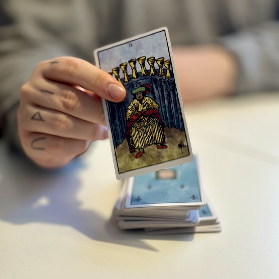 Ett tarotkort (Nio Bägare, Rider–Waite) hålls upp över leken.